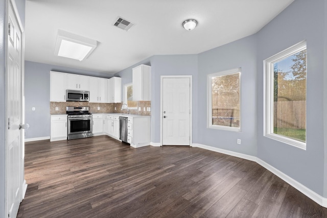 kitchen featuring appliances with stainless steel finishes, white cabinets, dark hardwood / wood-style flooring, decorative backsplash, and a healthy amount of sunlight