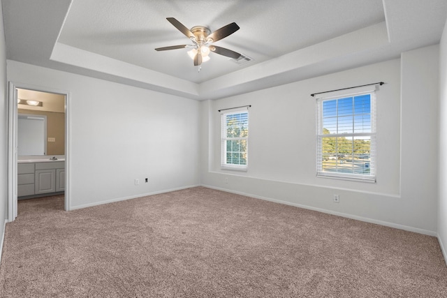 unfurnished bedroom with a raised ceiling, connected bathroom, light carpet, and a textured ceiling