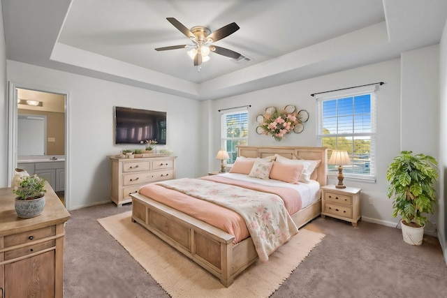 bedroom featuring ensuite bathroom, light colored carpet, ceiling fan, and a tray ceiling