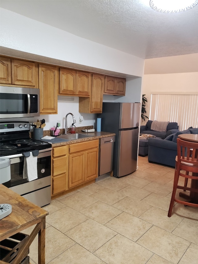 kitchen with light tile patterned flooring, appliances with stainless steel finishes, sink, and a textured ceiling