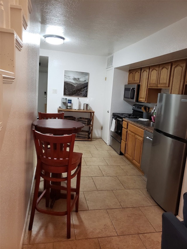 kitchen with light tile patterned floors, stainless steel appliances, and a textured ceiling