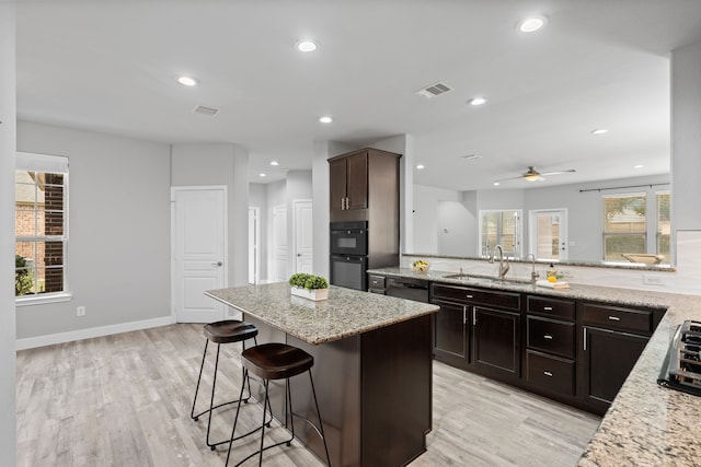 kitchen featuring dark brown cabinetry, sink, a breakfast bar area, light stone counters, and a kitchen island