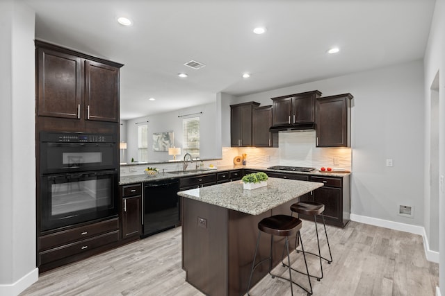 kitchen featuring a kitchen island, sink, backsplash, a kitchen bar, and black appliances