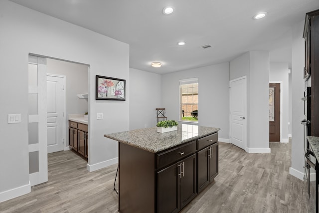 kitchen featuring light stone countertops, dark brown cabinets, light hardwood / wood-style floors, and a kitchen island