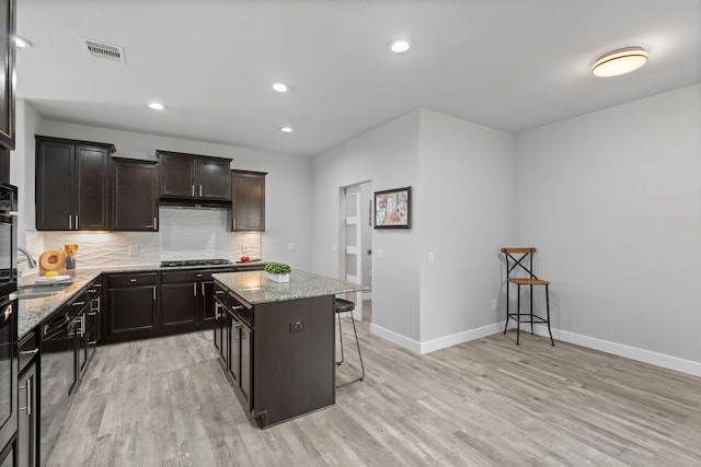 kitchen featuring decorative backsplash, a kitchen island, light hardwood / wood-style floors, and a breakfast bar area