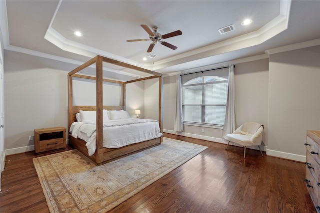 bedroom featuring dark wood-type flooring, visible vents, baseboards, ornamental molding, and a tray ceiling