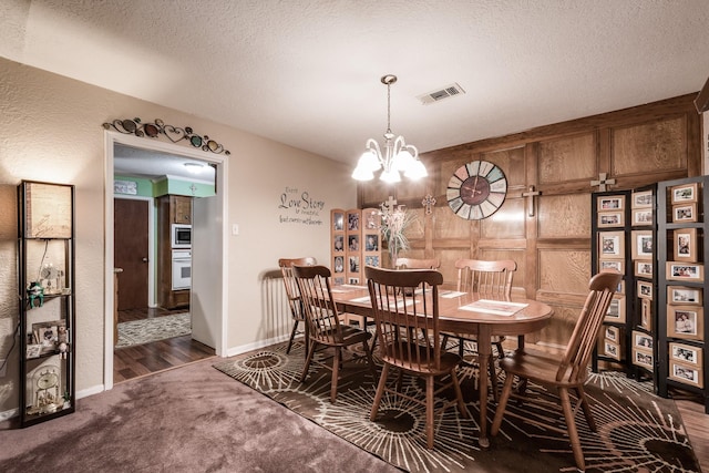 dining space featuring an inviting chandelier, wood walls, a textured ceiling, and dark colored carpet