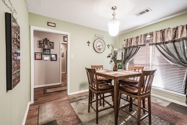 dining area with a textured ceiling, wood finished floors, visible vents, and baseboards