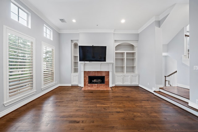 unfurnished living room with crown molding, dark hardwood / wood-style flooring, a tile fireplace, and built in features