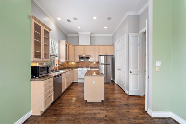 kitchen with sink, appliances with stainless steel finishes, dark stone countertops, a center island, and decorative backsplash