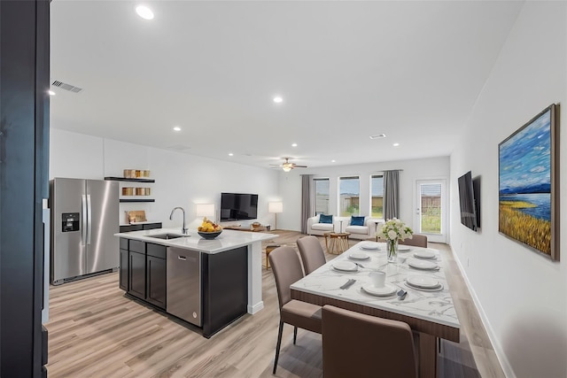 kitchen with sink, light hardwood / wood-style flooring, ceiling fan, appliances with stainless steel finishes, and an island with sink