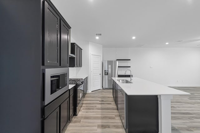 kitchen with stainless steel appliances, sink, a center island with sink, and light hardwood / wood-style floors