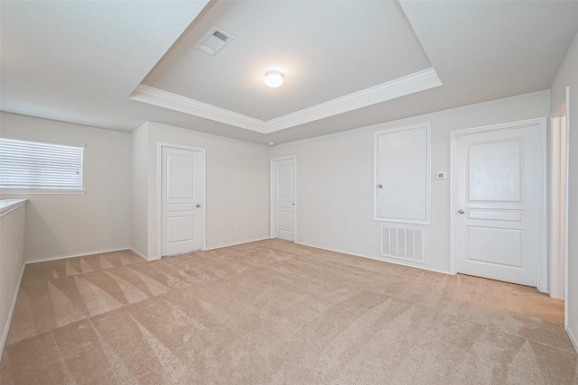 unfurnished bedroom featuring a tray ceiling, light carpet, visible vents, and crown molding