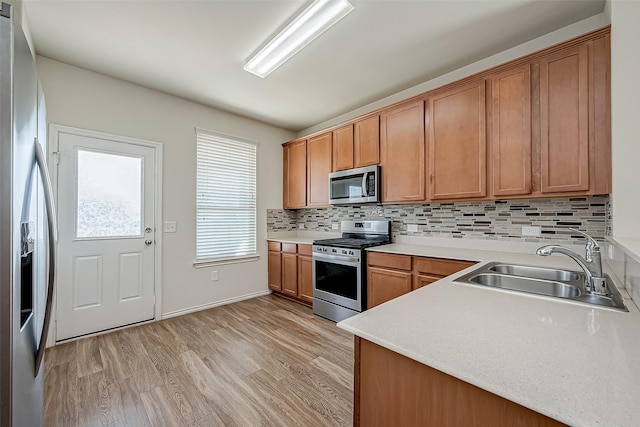 kitchen with light wood-type flooring, a sink, stainless steel appliances, light countertops, and decorative backsplash