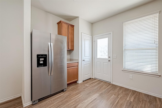 kitchen with brown cabinetry, stainless steel fridge, light wood-type flooring, and baseboards