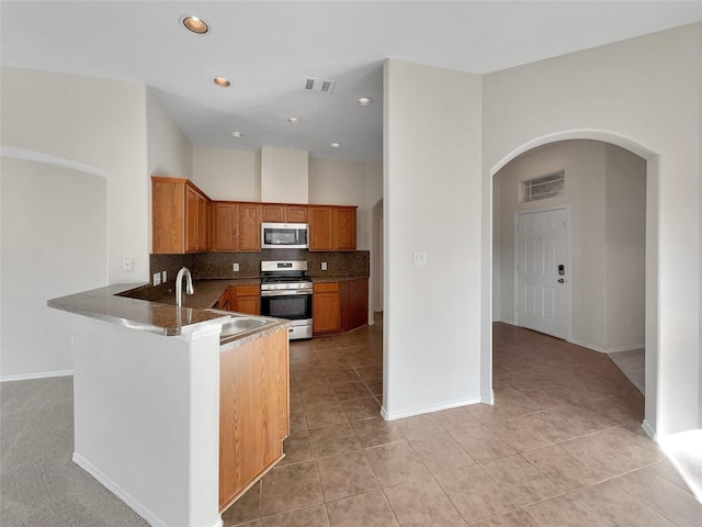 kitchen featuring sink, light tile patterned floors, appliances with stainless steel finishes, kitchen peninsula, and backsplash