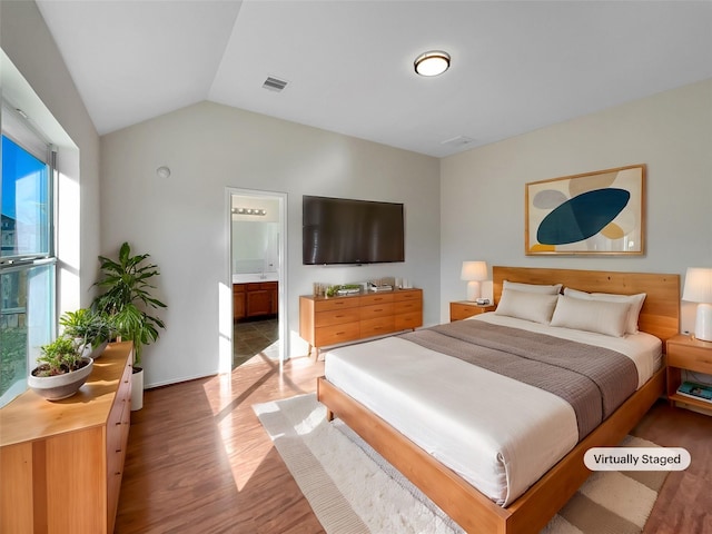 bedroom with vaulted ceiling, hardwood / wood-style floors, and ensuite bath