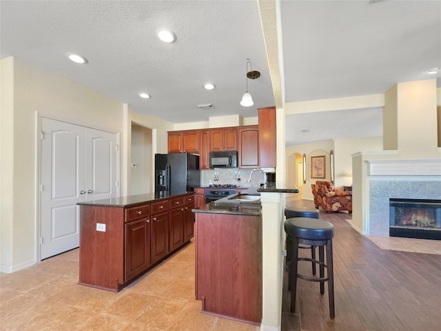 kitchen featuring sink, kitchen peninsula, pendant lighting, a tiled fireplace, and black appliances