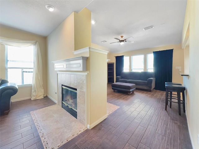 living room with a tiled fireplace, vaulted ceiling, plenty of natural light, and ceiling fan