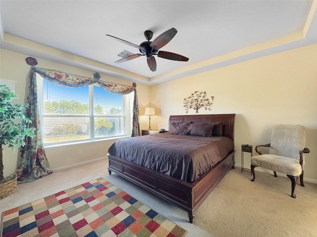 carpeted bedroom with a raised ceiling and ceiling fan