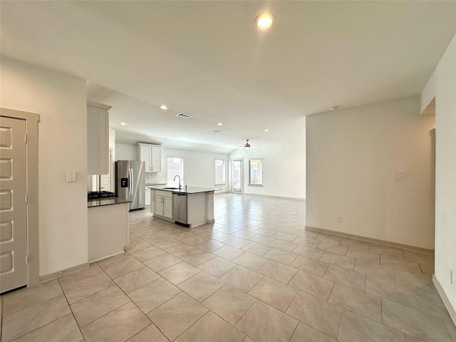 interior space featuring light tile patterned flooring, appliances with stainless steel finishes, white cabinetry, an island with sink, and sink