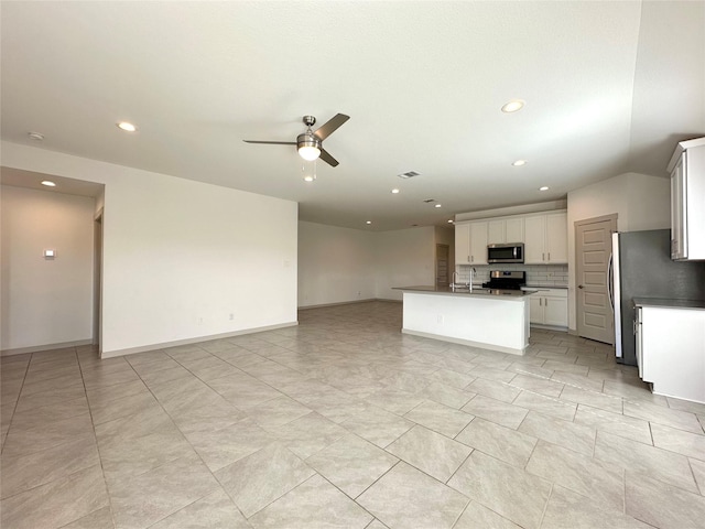 kitchen featuring ceiling fan, appliances with stainless steel finishes, white cabinetry, an island with sink, and decorative backsplash