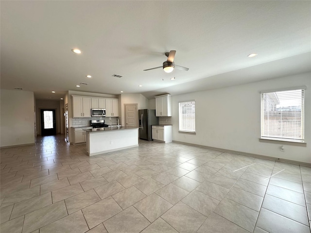 kitchen featuring ceiling fan, a kitchen island with sink, white cabinetry, stainless steel appliances, and decorative backsplash