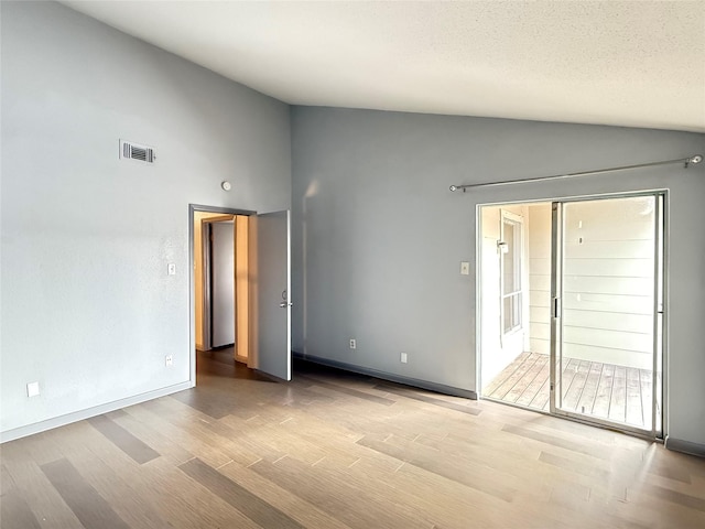 empty room with lofted ceiling, a textured ceiling, and light wood-type flooring