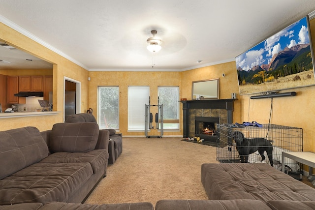 living room with a tiled fireplace, crown molding, ceiling fan, and carpet