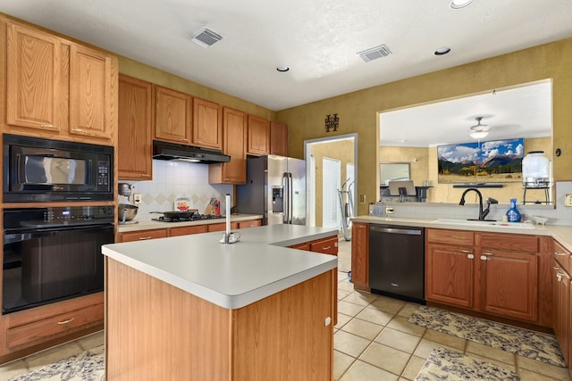 kitchen with sink, light tile patterned floors, tasteful backsplash, black appliances, and an island with sink