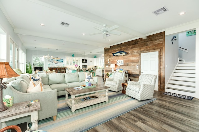 living room featuring ceiling fan with notable chandelier, wood walls, hardwood / wood-style flooring, ornamental molding, and beam ceiling