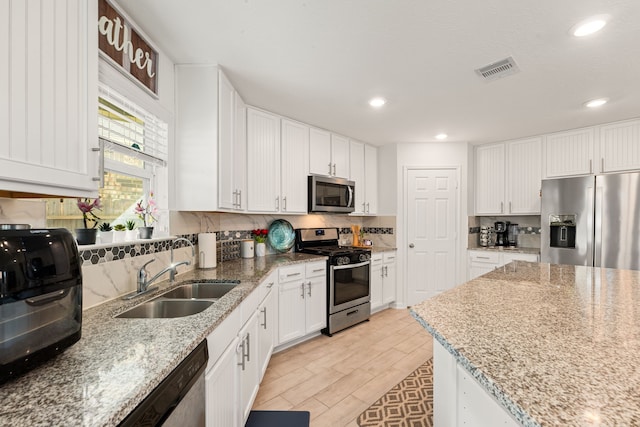 kitchen featuring sink, appliances with stainless steel finishes, tasteful backsplash, light stone countertops, and white cabinets