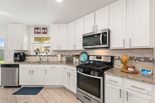 kitchen with sink, appliances with stainless steel finishes, white cabinetry, light stone counters, and tasteful backsplash