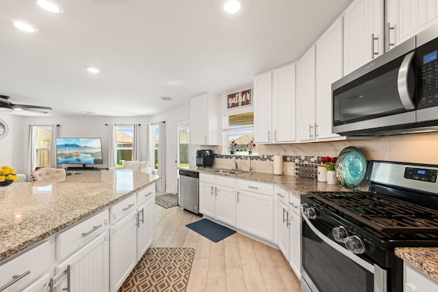 kitchen with white cabinetry, appliances with stainless steel finishes, light stone countertops, and backsplash