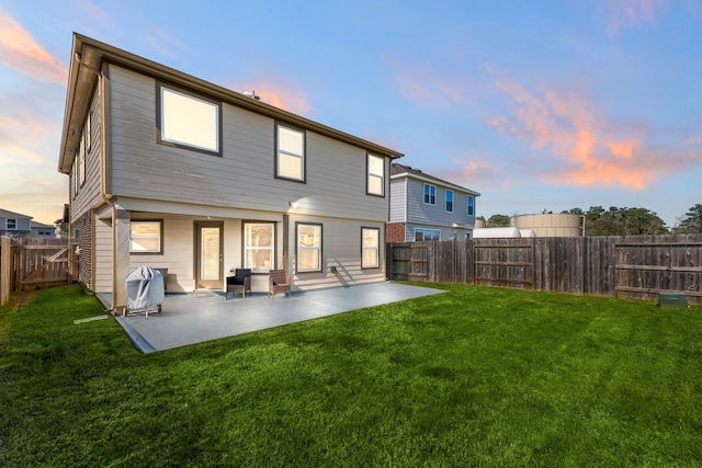 back house at dusk featuring a yard and a patio