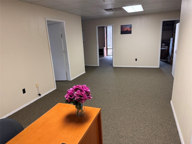 hall with a drop ceiling and dark carpet