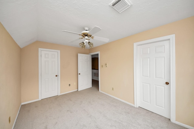 unfurnished bedroom featuring a textured ceiling, vaulted ceiling, light colored carpet, and ceiling fan