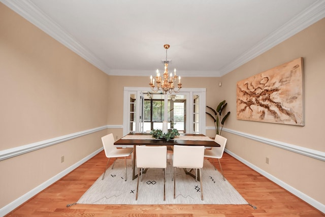 dining space with crown molding, an inviting chandelier, light wood-type flooring, and french doors