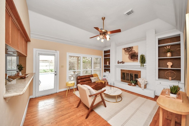 living room with a fireplace, light hardwood / wood-style flooring, ornamental molding, ceiling fan, and built in shelves