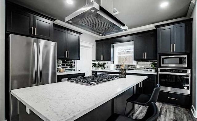 kitchen featuring wall chimney range hood, decorative backsplash, a center island, and appliances with stainless steel finishes