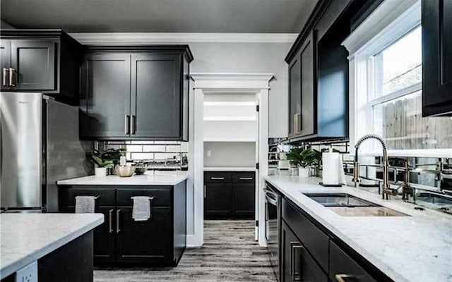 kitchen featuring sink, light stone counters, ornamental molding, stainless steel fridge, and light hardwood / wood-style floors