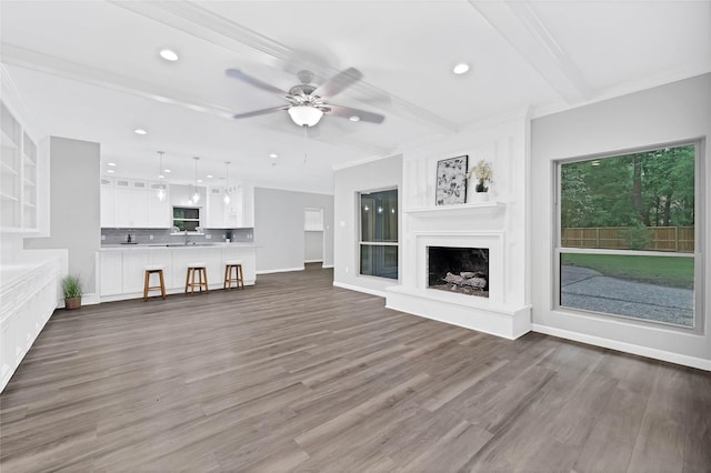 unfurnished living room featuring sink, ornamental molding, dark hardwood / wood-style flooring, beamed ceiling, and ceiling fan