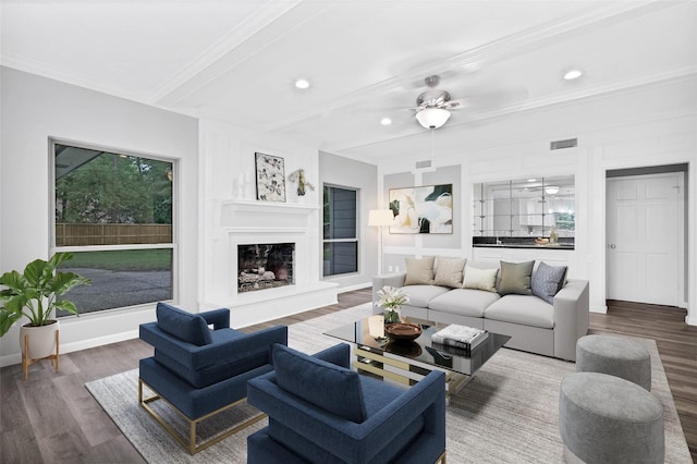 living room featuring beam ceiling, ornamental molding, hardwood / wood-style flooring, ceiling fan, and a fireplace