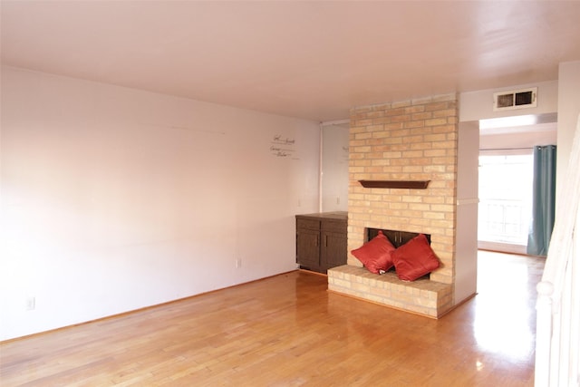 unfurnished living room featuring a brick fireplace and light wood-type flooring