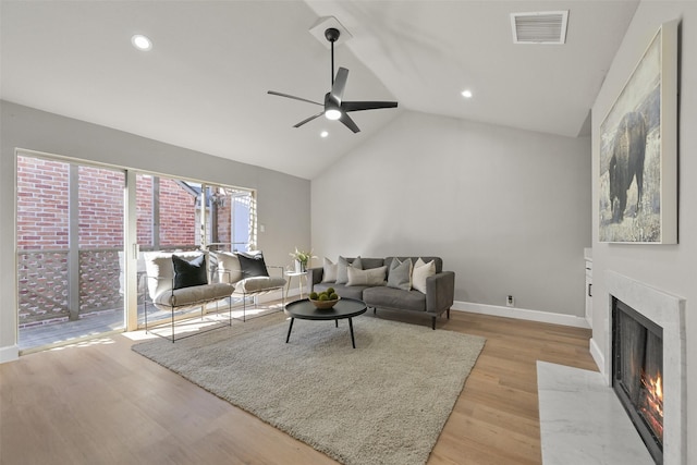 living room with vaulted ceiling, ceiling fan, a fireplace, and light hardwood / wood-style floors