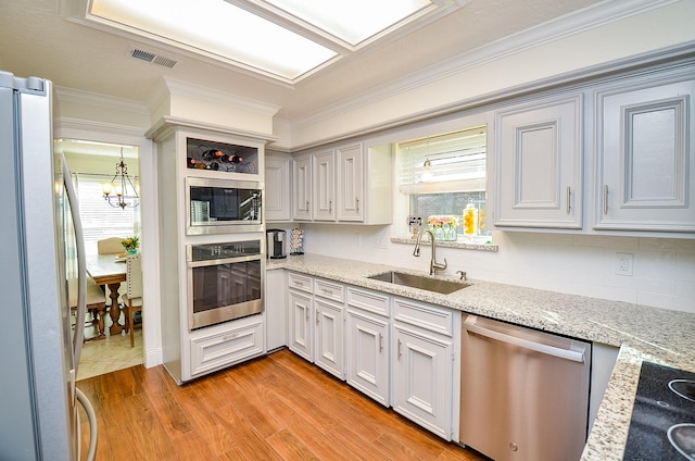 kitchen featuring decorative light fixtures, sink, stainless steel appliances, light stone countertops, and light hardwood / wood-style flooring