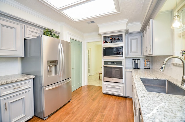 kitchen with pendant lighting, sink, stainless steel appliances, light stone counters, and light wood-type flooring