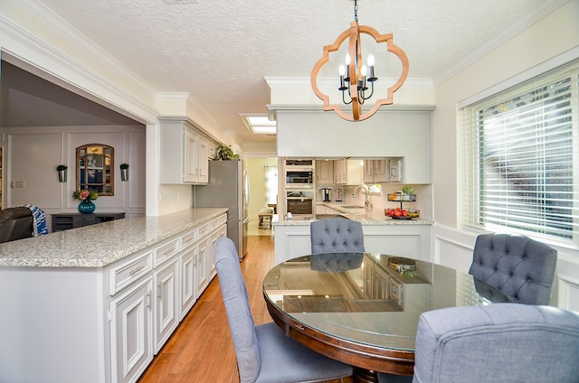 dining space with sink, a chandelier, ornamental molding, a textured ceiling, and light hardwood / wood-style flooring