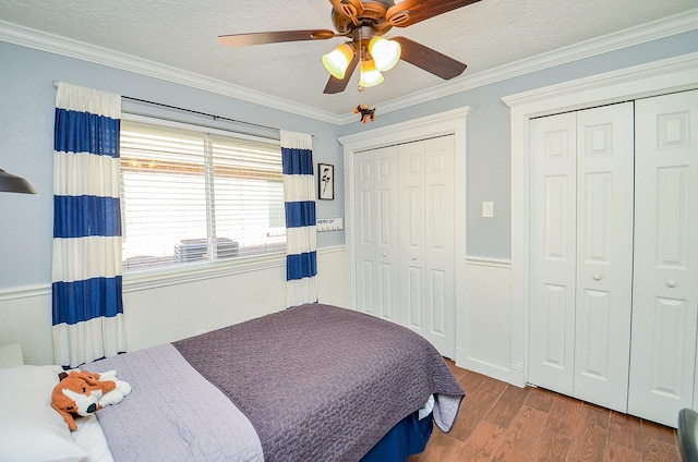 bedroom featuring two closets, hardwood / wood-style flooring, ceiling fan, crown molding, and a textured ceiling