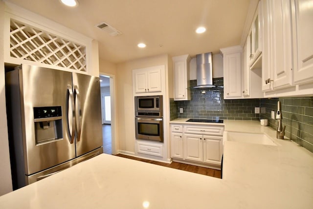 kitchen with sink, appliances with stainless steel finishes, tasteful backsplash, white cabinets, and wall chimney exhaust hood